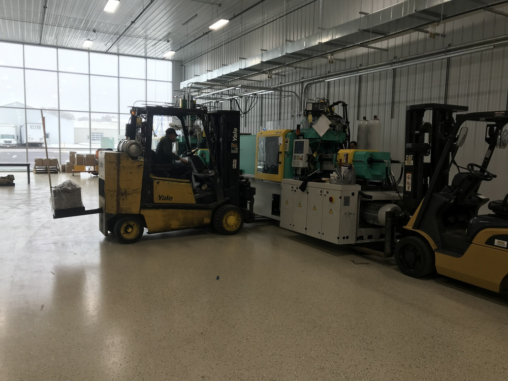 Forklifts positioning an injection molding machine inside the new facility