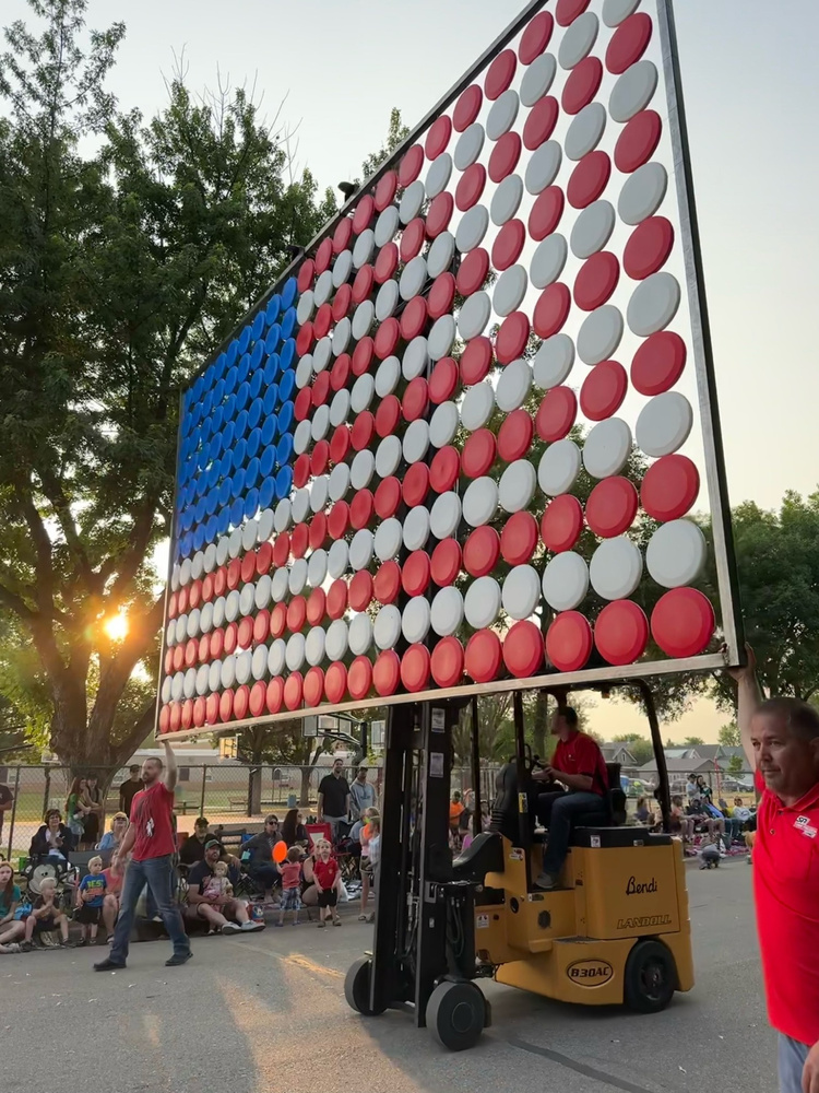 A forklift carries a giant American flag made from red, white, and blue frisbees along the Paynesville parade route