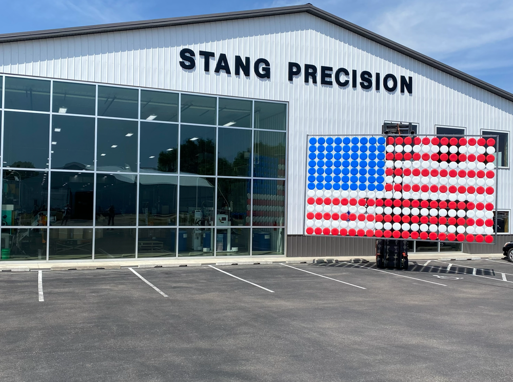Stang Precision’s Paynesville facility with a large American flag assembled from red, white, and blue molded pieces